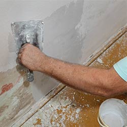 Man smoothing over wall damage with a trowel